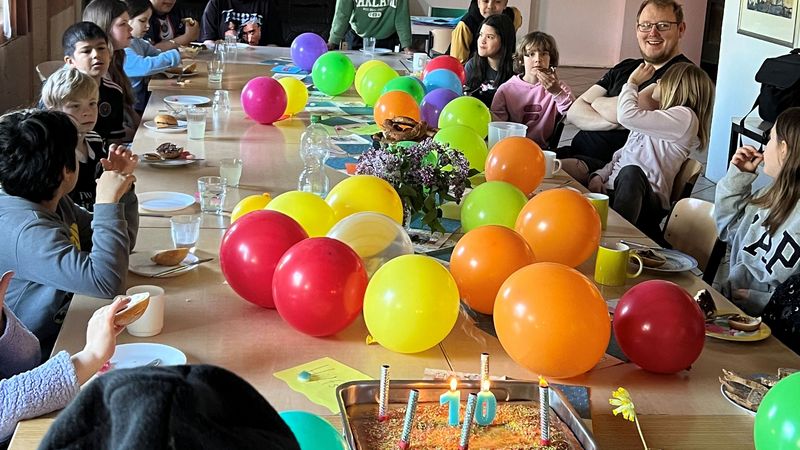 Frühstück der Kinderzeitgruppe mit einem Geburtstagskuchen und Luftballons.