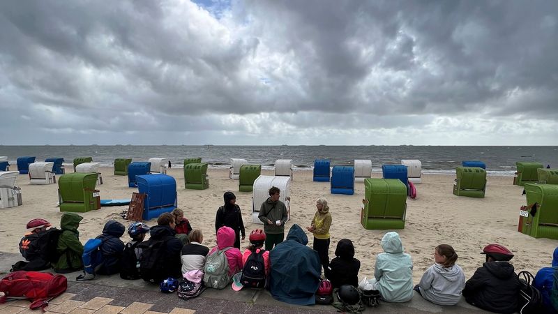 Kinder sitzen am Strand, das Wetter ist sonnig und stürmisch.