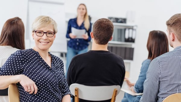 Eine Frau sitzt im Unterricht, dreht sich um und lächelt.