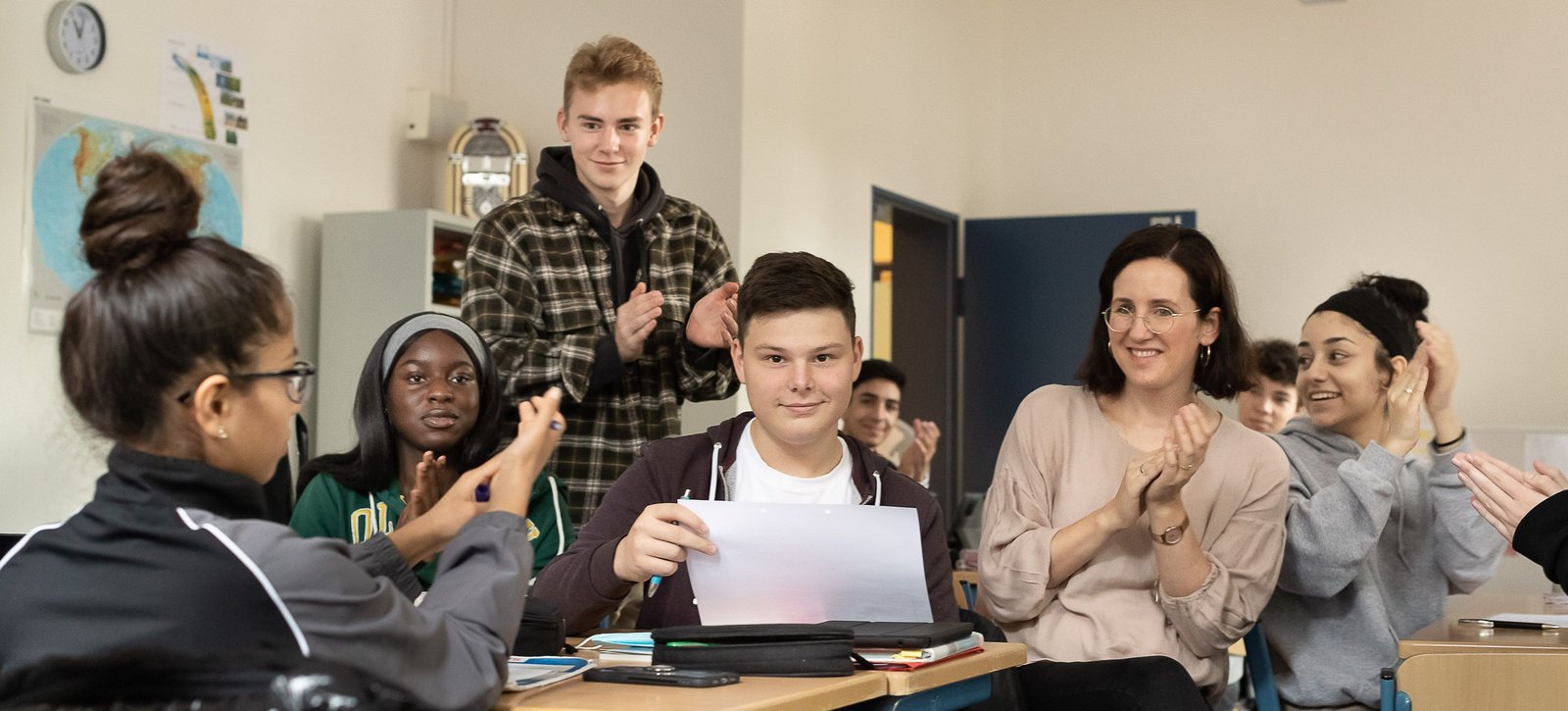 Schülerinnen und Schüler sitzen zusammen mit ihrer Lehrerin am Tisch.