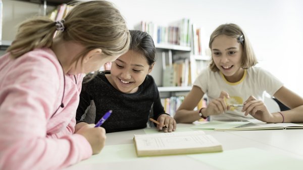 Drei Mädchen sitzen am Tisch und machen zusammen Hausaufgaben.